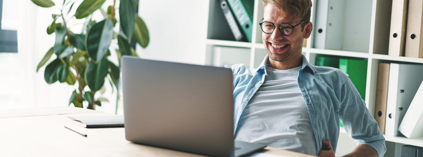 Smiling young man working at home. Happy social distancing concept. Use laptop for new job search. Blurred background